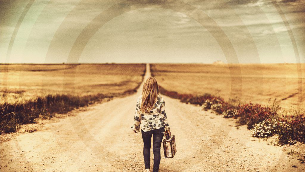 A woman is walking down a dirt road holding a lantern.