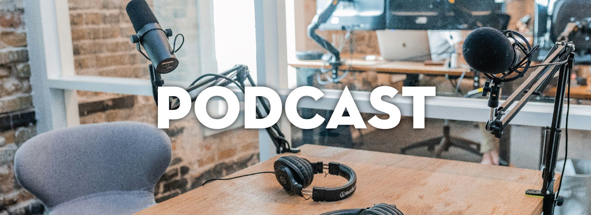 Two microphones on boom arms and a pair of headphones on a wooden table, with 