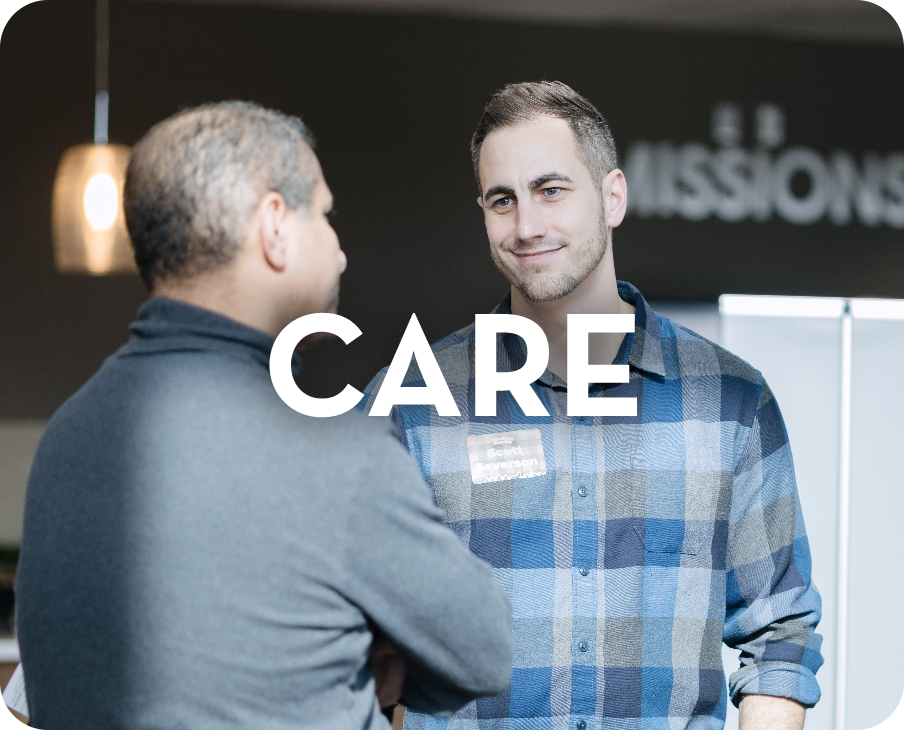 Two men are talking to each other in front of a sign that says care