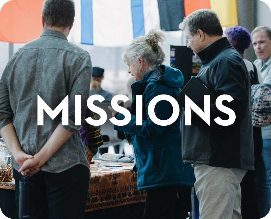 A group of people standing in front of a table with the word missions on it