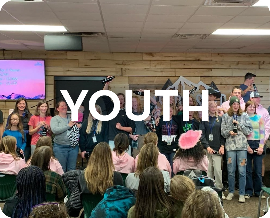 A group of young people are standing in front of a large group of people in a room.