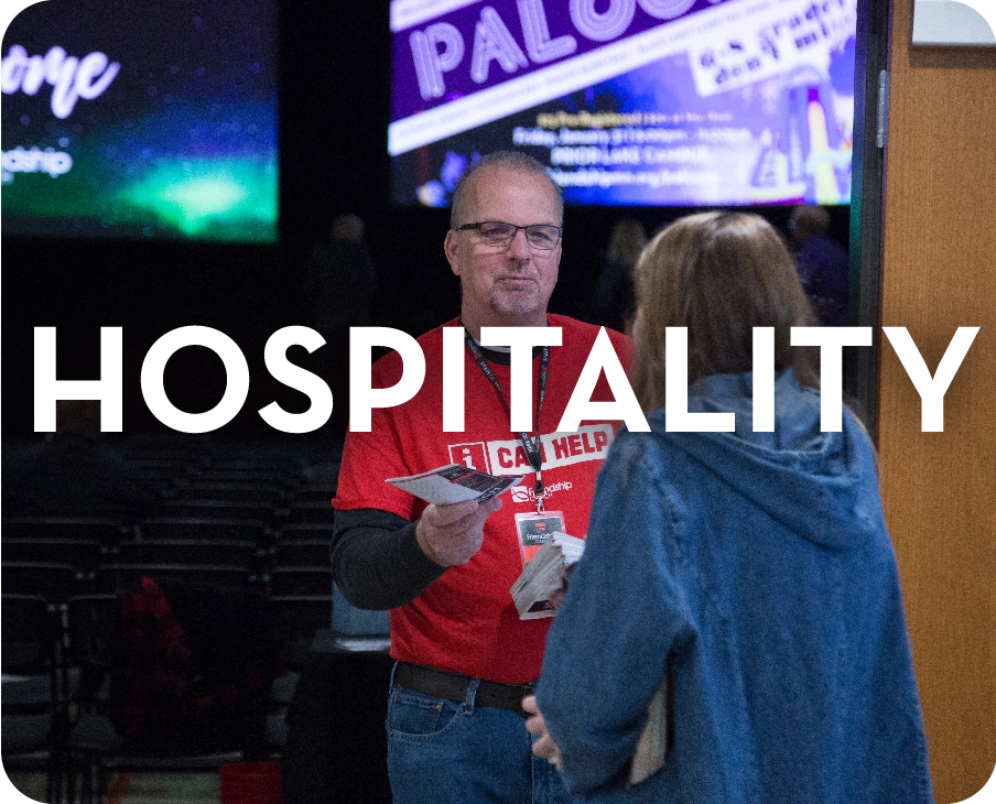 A man in a red shirt is talking to a woman in front of a sign that says hospitality