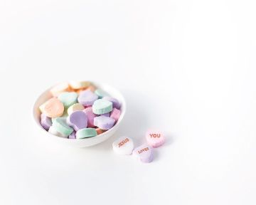 A bowl of candy hearts with messages on them on a white background.
