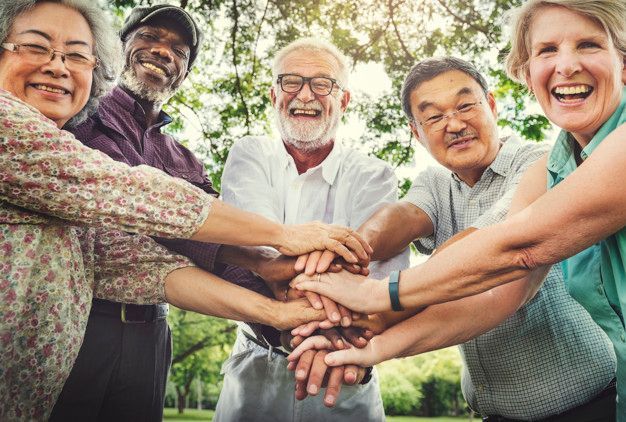 A group of elderly people are putting their hands together in a circle.