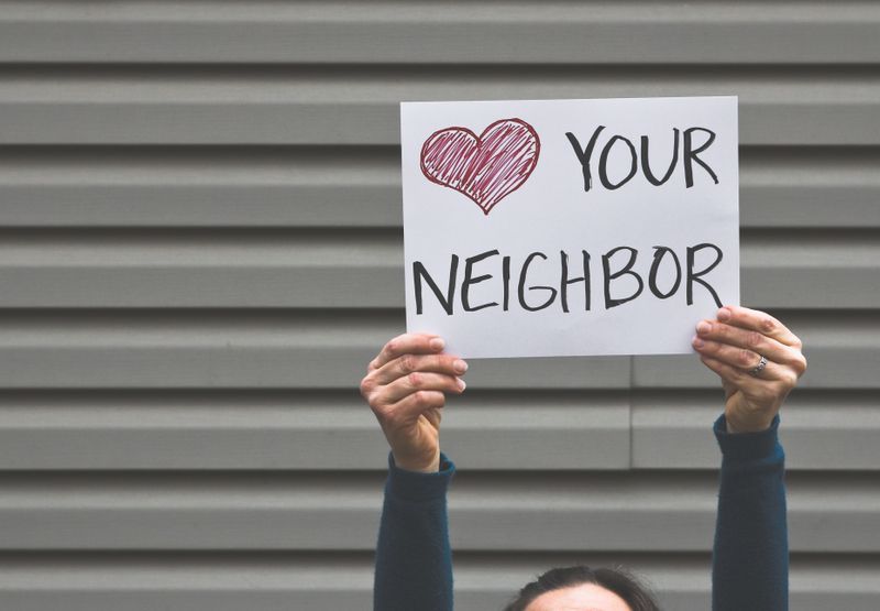 A woman is holding a sign that says `` i love your neighbor ''.