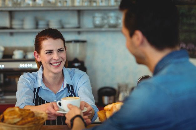 A woman is serving a cup of coffee to a man in a cafe.