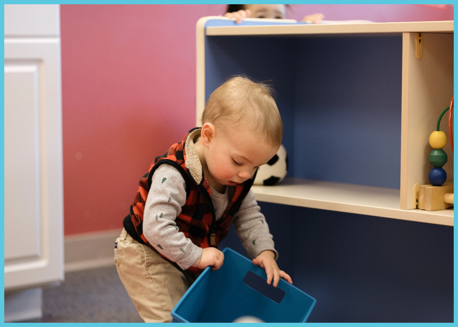 A baby is playing with a blue box in a room