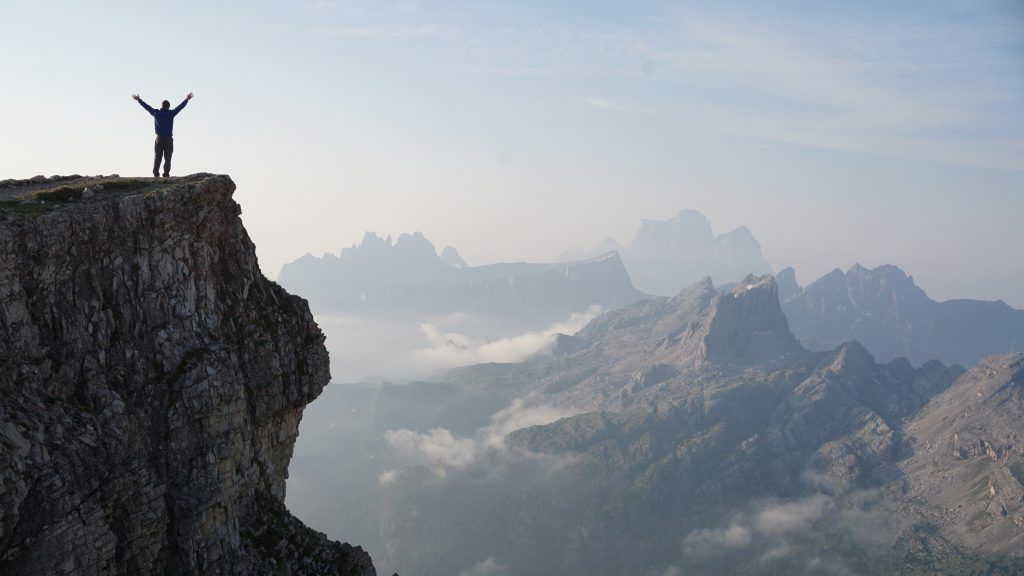 A man is standing on the edge of a cliff with his arms in the air.