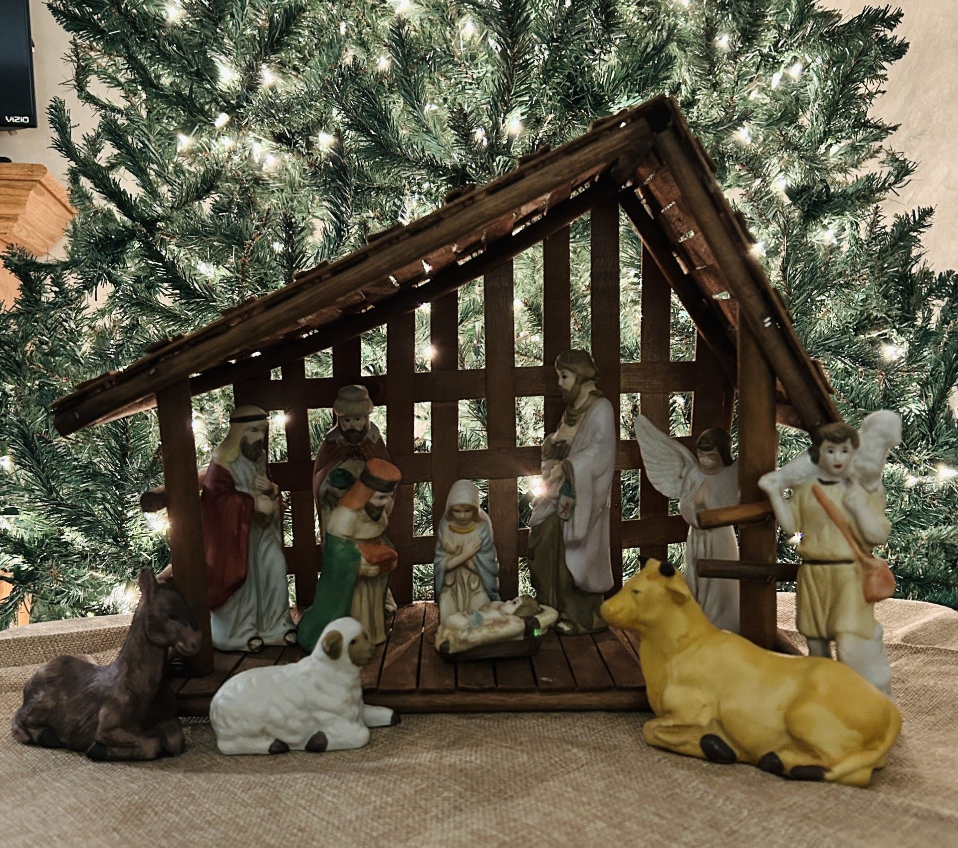 A Nativity set arranged in a wooden stable with figures of the Holy Family, angels, and animals before a lit tree.