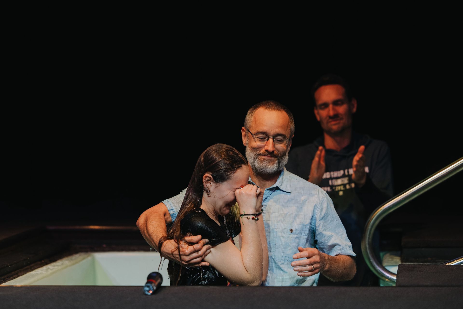 A man is baptizing a woman in a pool.
