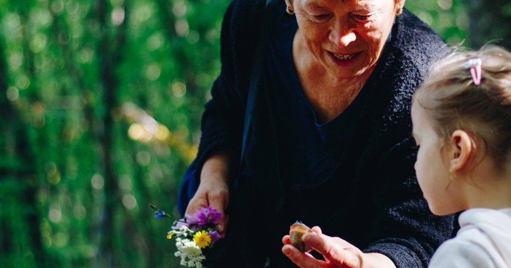 An elderly woman is giving a flower to a little girl.