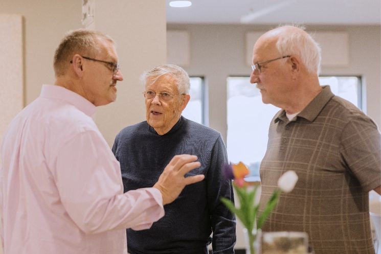 Three older men are talking to each other in a room.