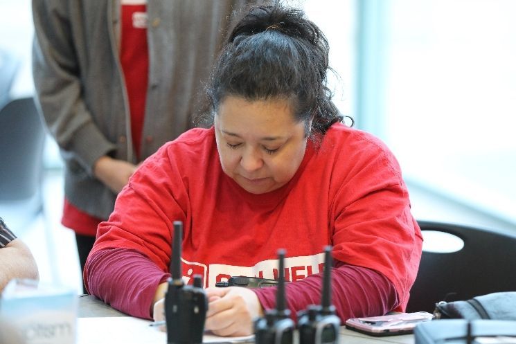 A woman in a red shirt is sitting at a table using a walkie talkie.