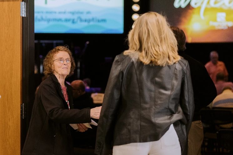 A woman in a leather jacket is talking to another woman in a room.