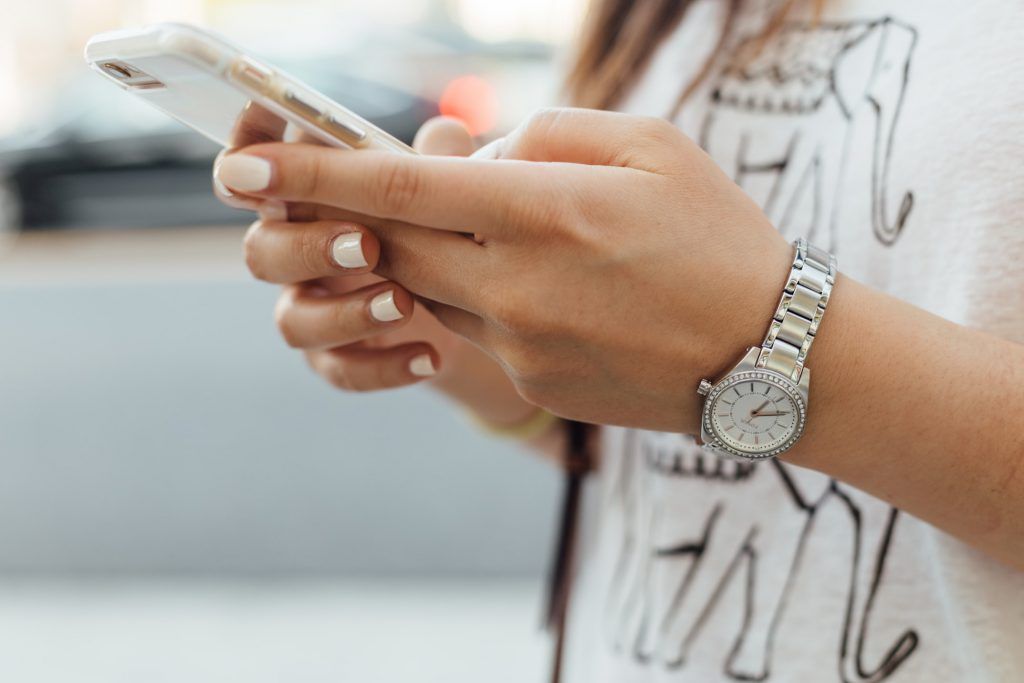 A woman wearing a watch is holding a cell phone in her hands.