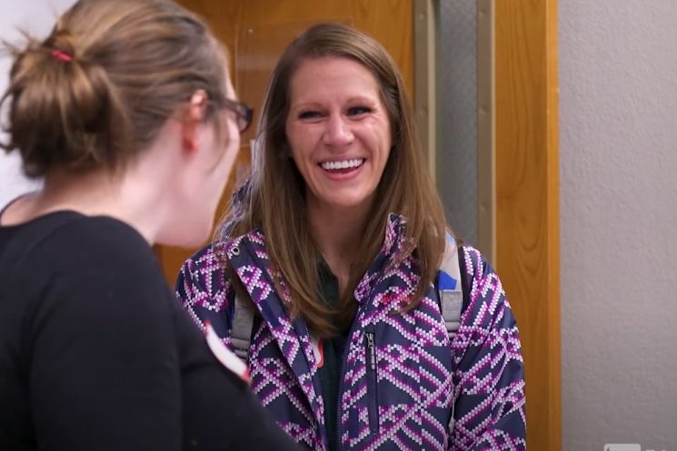A woman in a purple jacket is smiling while talking to another woman.