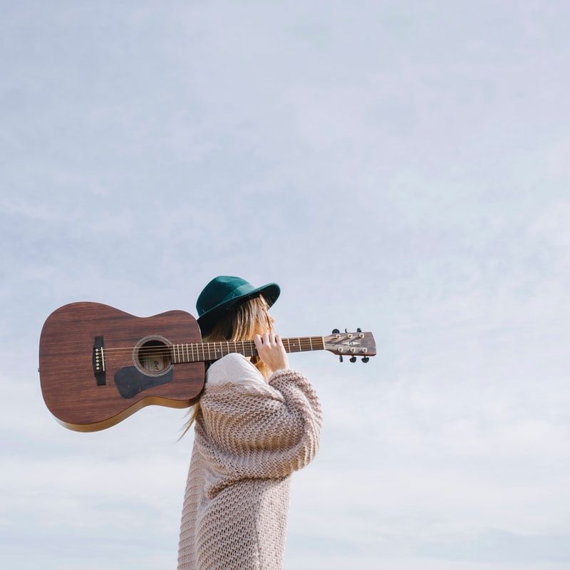A woman is holding an acoustic guitar over her shoulder.