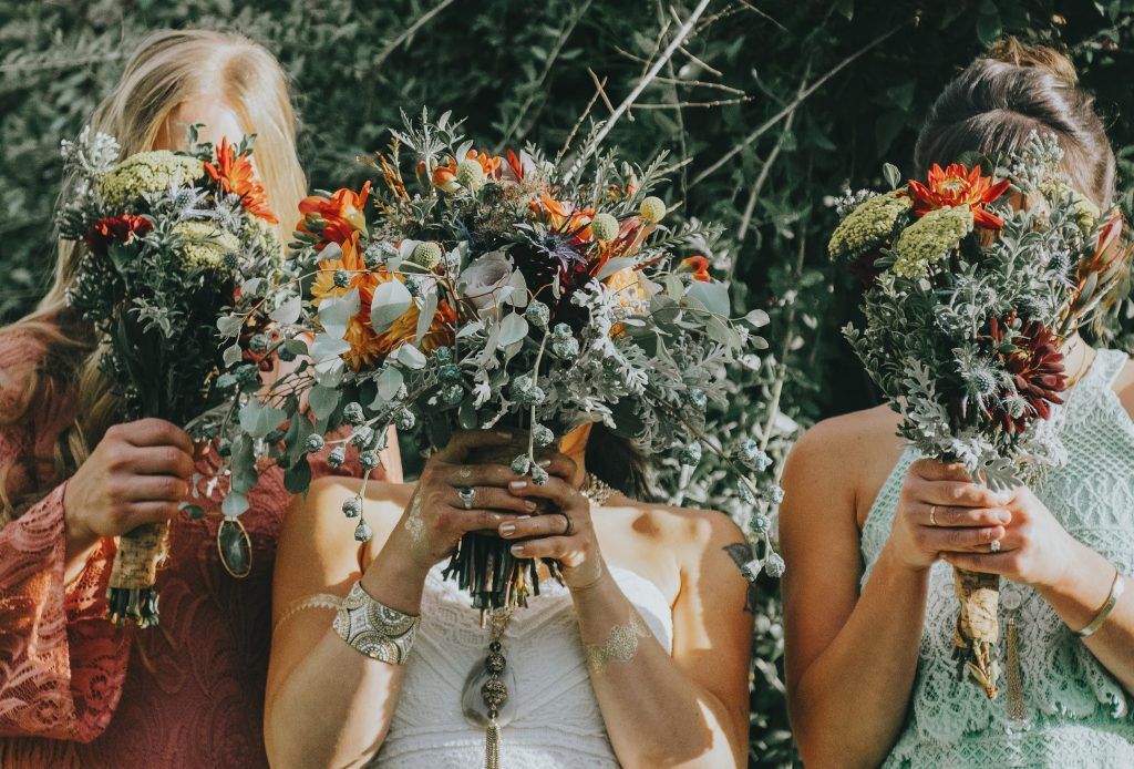 A bride and her bridesmaids are holding bouquets of flowers in front of their faces.