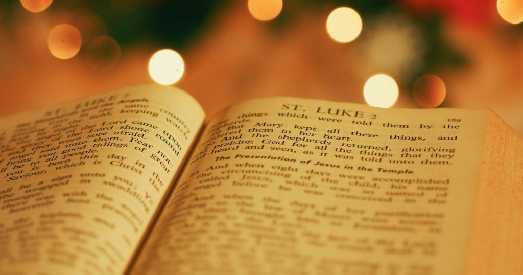 A close up of an open bible with christmas lights in the background.