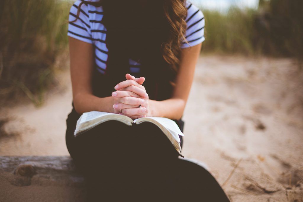 A woman is sitting on a bench with her hands folded over a bible.