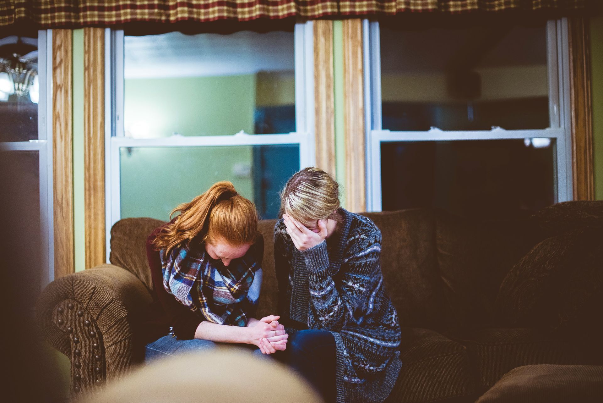 A man and a woman are sitting on a couch in front of a window.