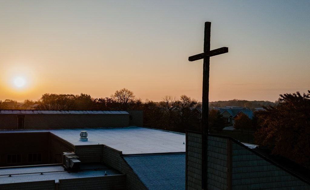 A cross is standing on top of a building at sunset.