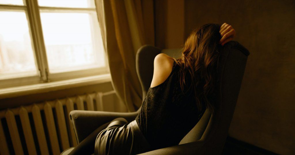 A woman is sitting in a chair in front of a window.