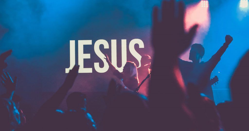 A group of people are raising their hands in the air in front of a sign that says jesus.