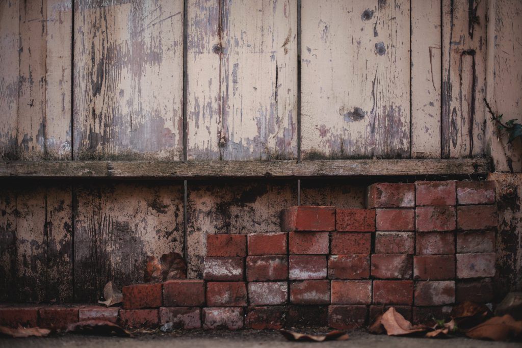 A brick wall with a wooden fence in the background.