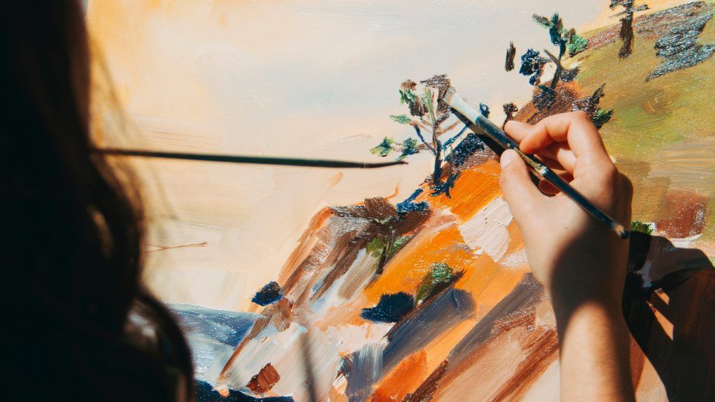 A woman is painting a landscape with a brush on a canvas.