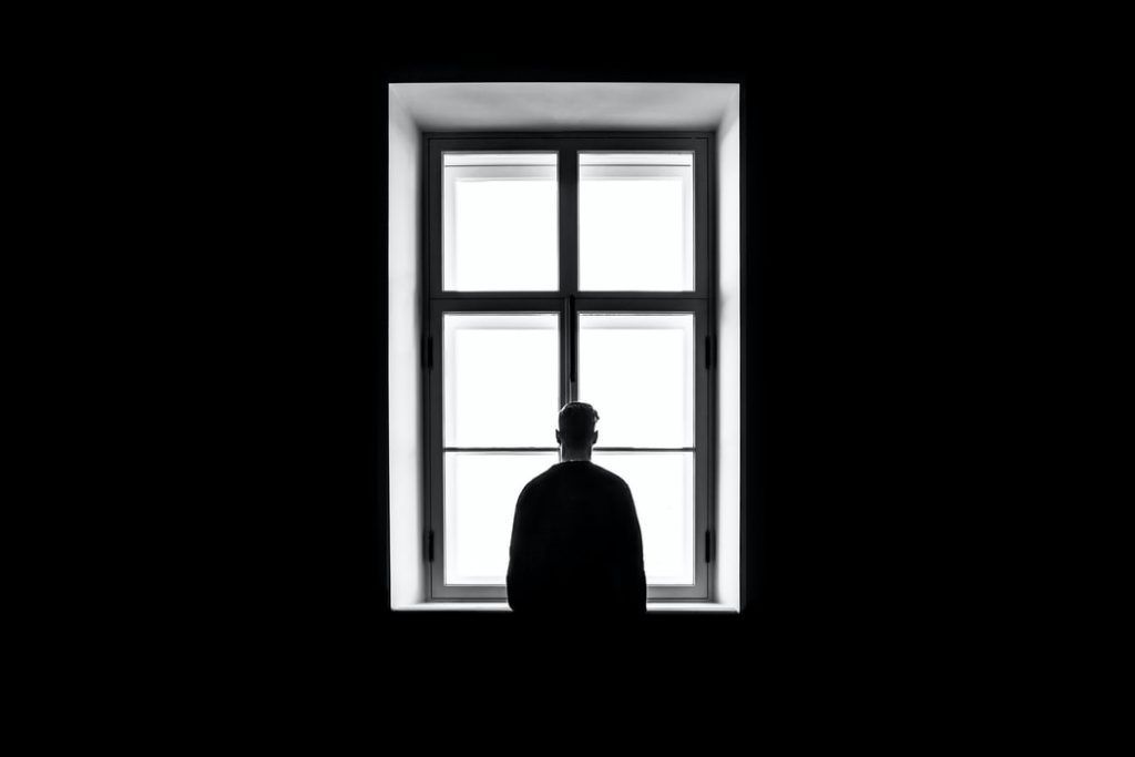 A man in a hat is looking out of a window in a dark room.