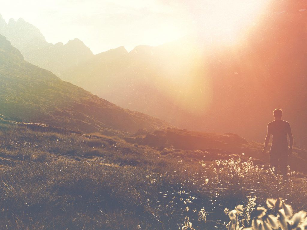 A man is standing in a field with mountains in the background.