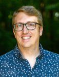A man wearing glasses and a blue shirt is smiling for the camera.