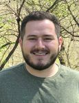 A man with a beard is smiling for the camera while wearing a green shirt.