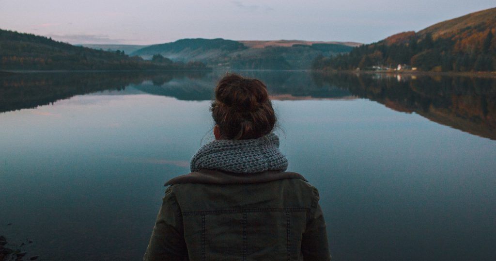 A woman is standing on a cliff overlooking a lake.
