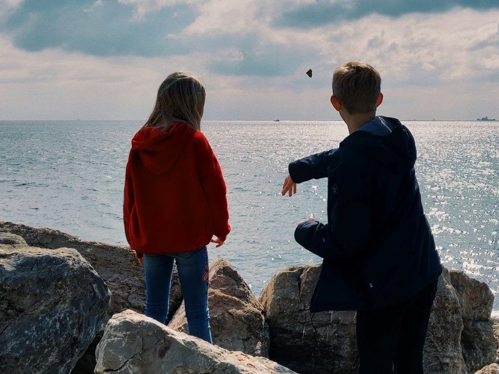 A boy and a girl are sitting on rocks looking at the ocean.