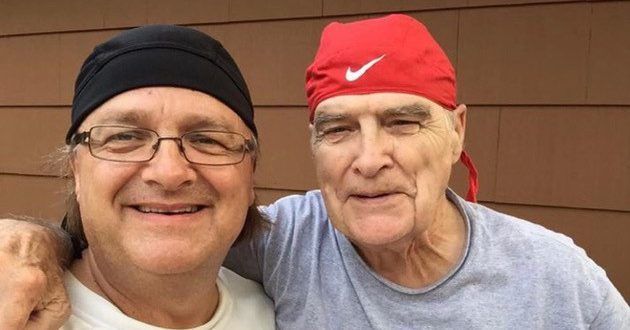 Two men are posing for a picture together and one of them is wearing a red nike hat.