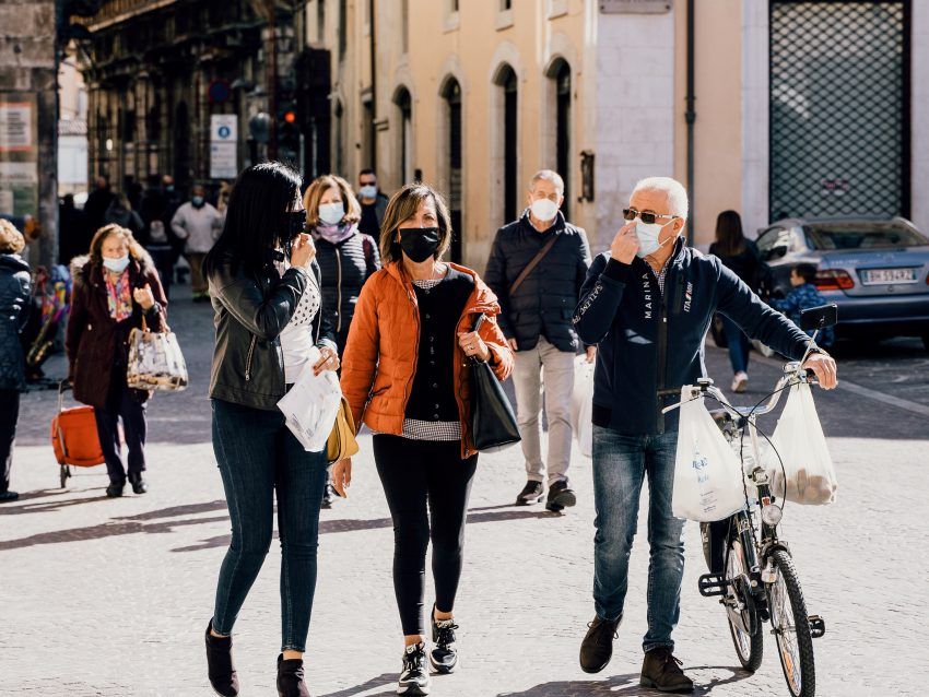 A group of people wearing face masks are walking down a street.
