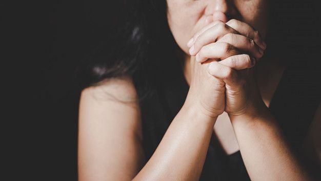 A woman is praying with her hands folded in front of her face.