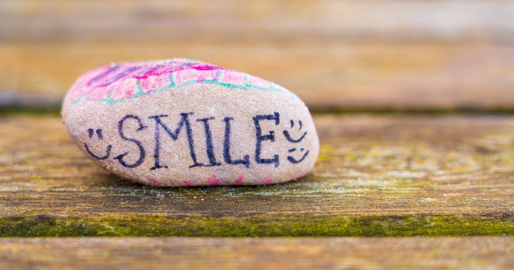 A rock with the word smile written on it is sitting on a wooden table.