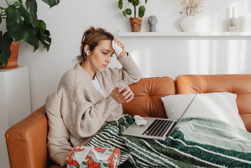 A woman is sitting on a couch with a laptop and a napkin.