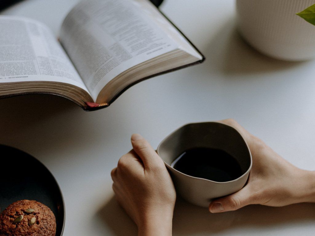 A person is holding a cup of coffee and reading a bible.