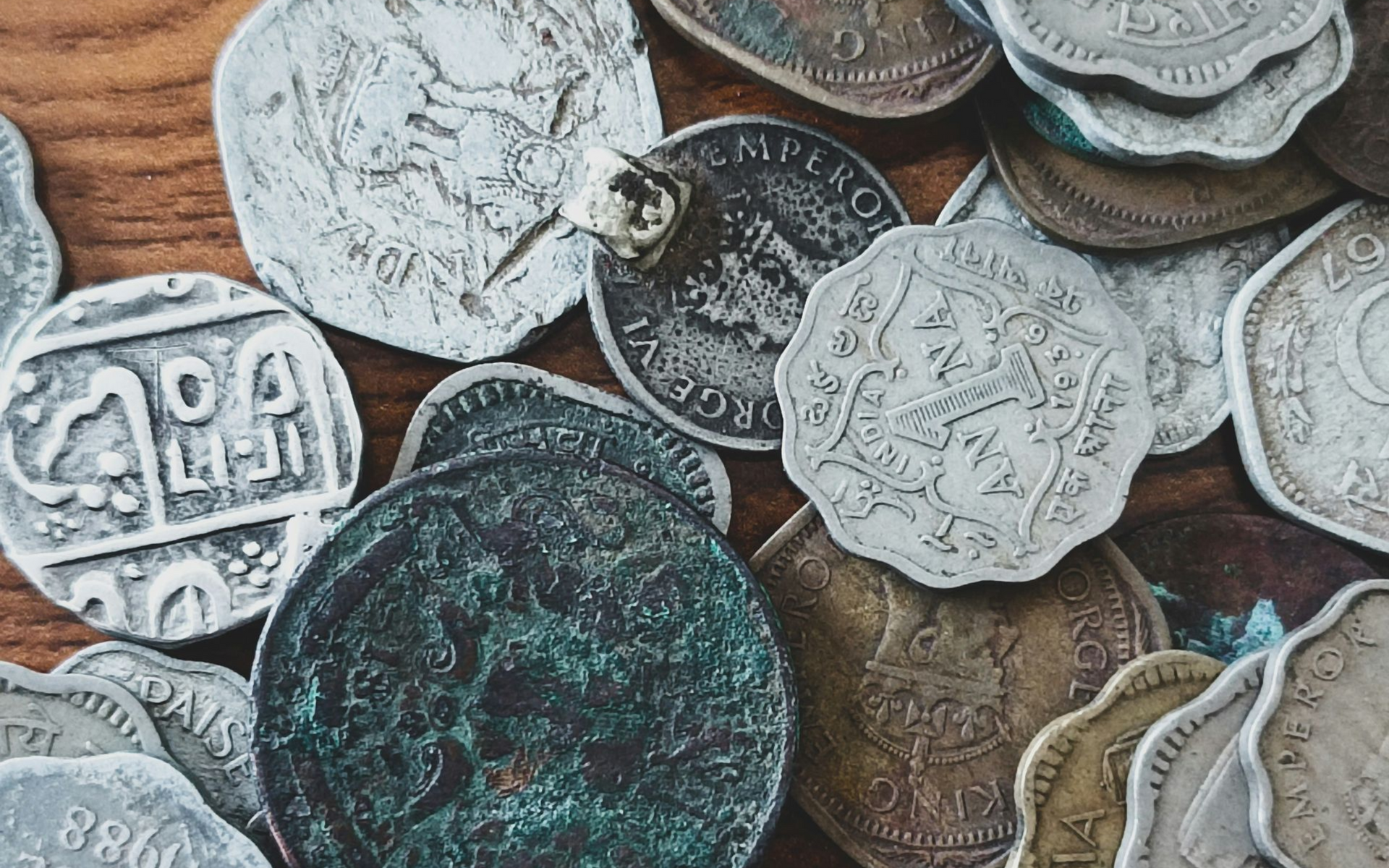 A collection of assorted vintage and oxidized metal coins scattered across a wooden surface.