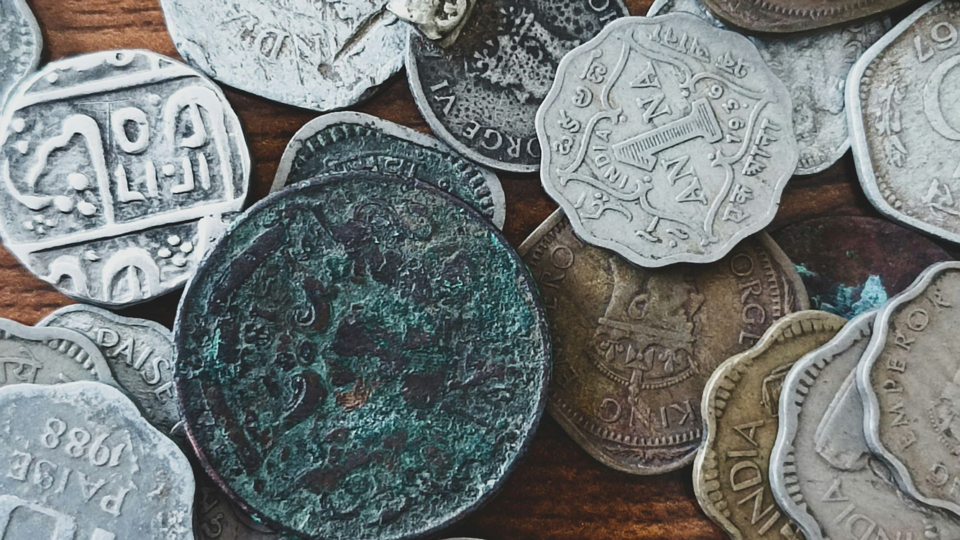 A collection of various vintage and weathered metal coins scattered on a wooden surface.