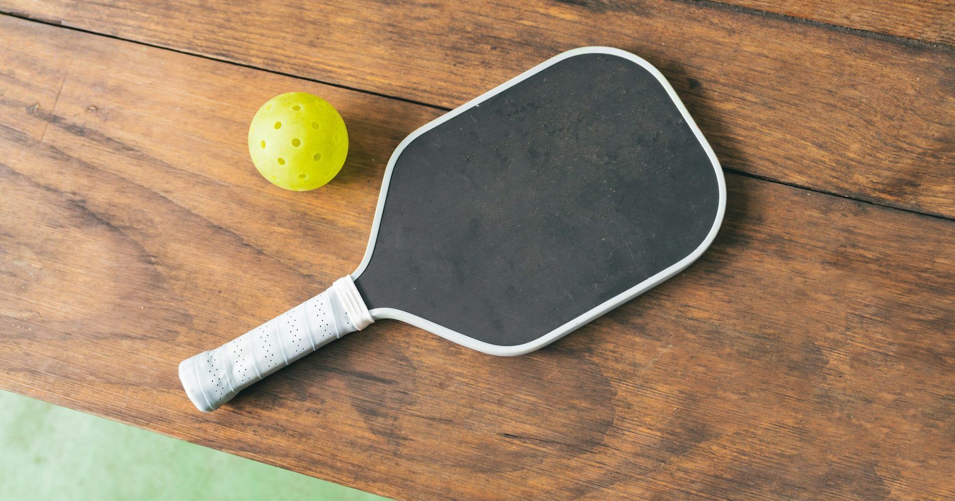 A paddle and a ball are on a wooden table.