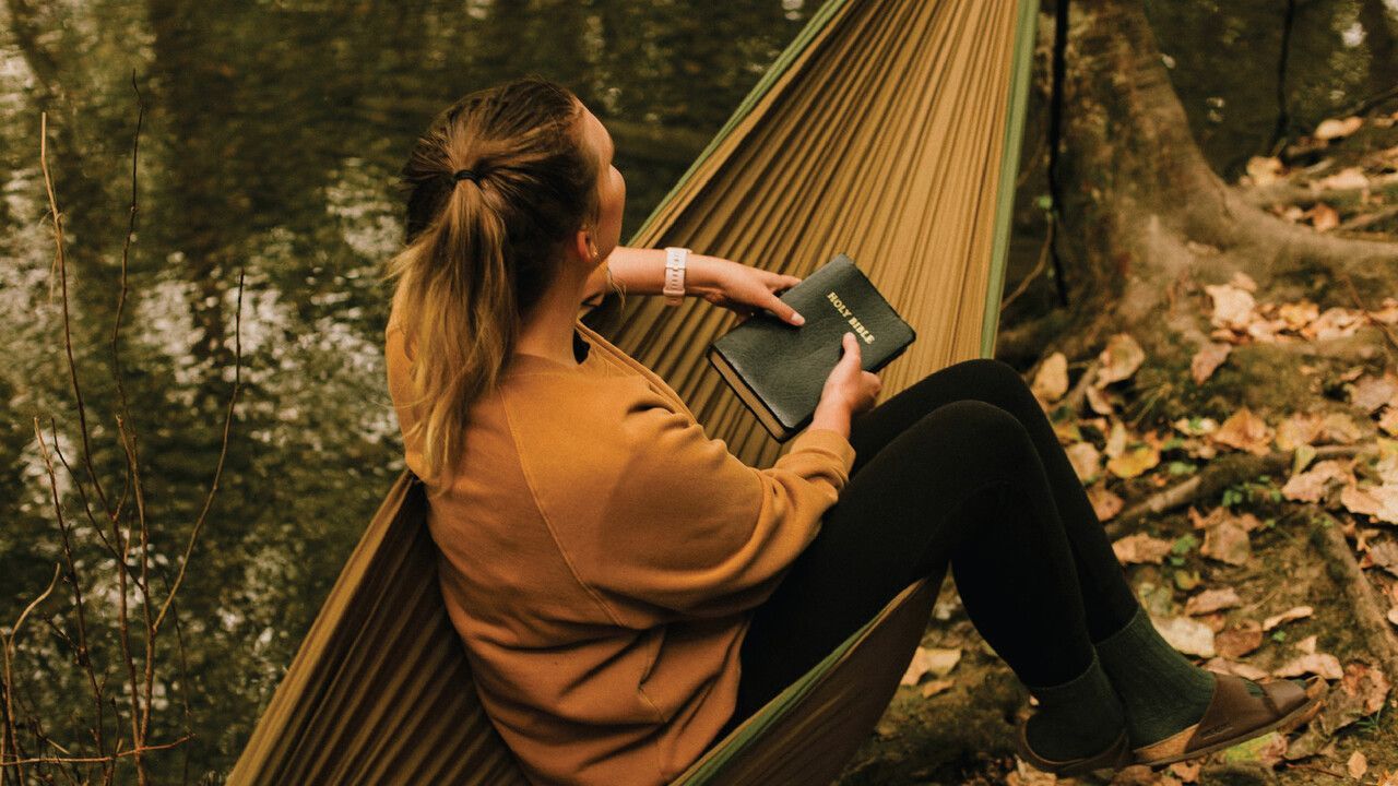 A woman is sitting in a hammock reading a book.