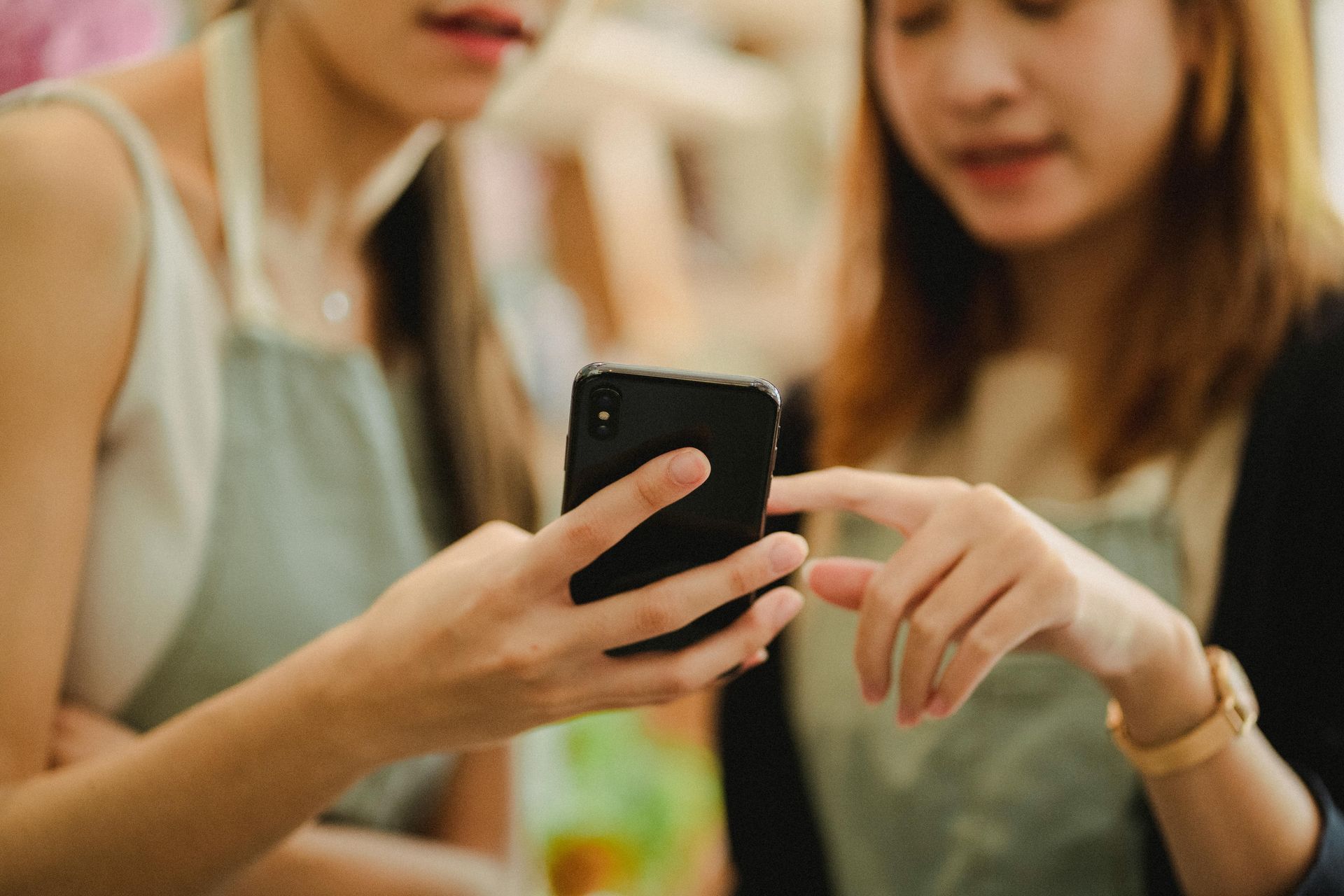 Duas mulheres olham para um smartphone; uma delas aponta para a tela. Ambas usam aventais.
