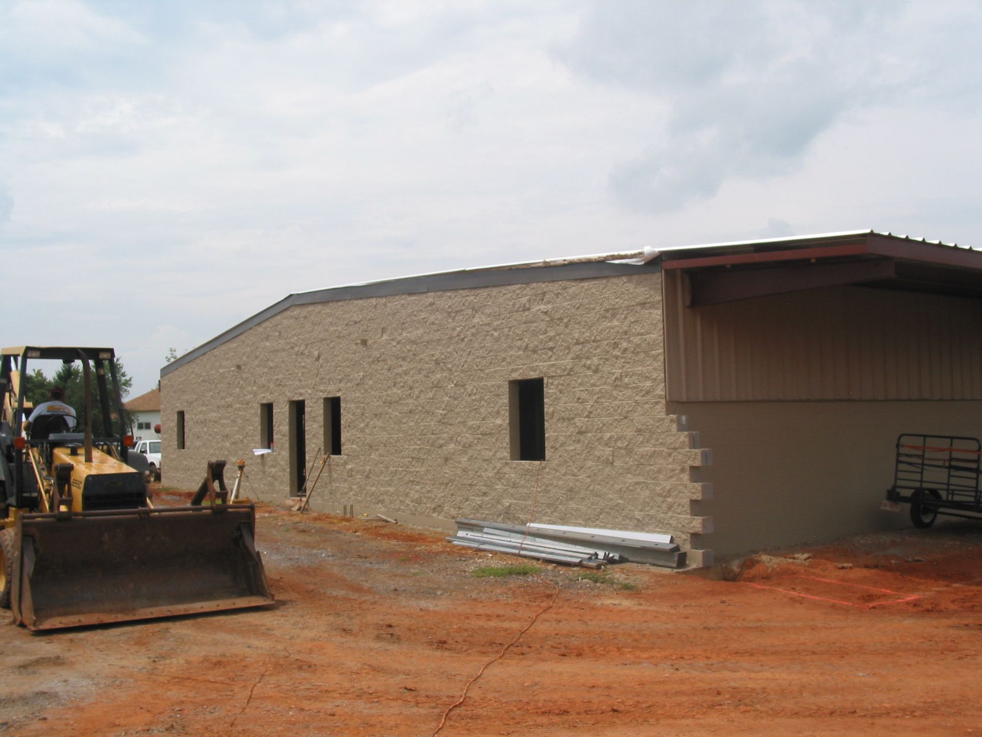 Construction site with tan building, bulldozer, and stacked materials on red dirt.
