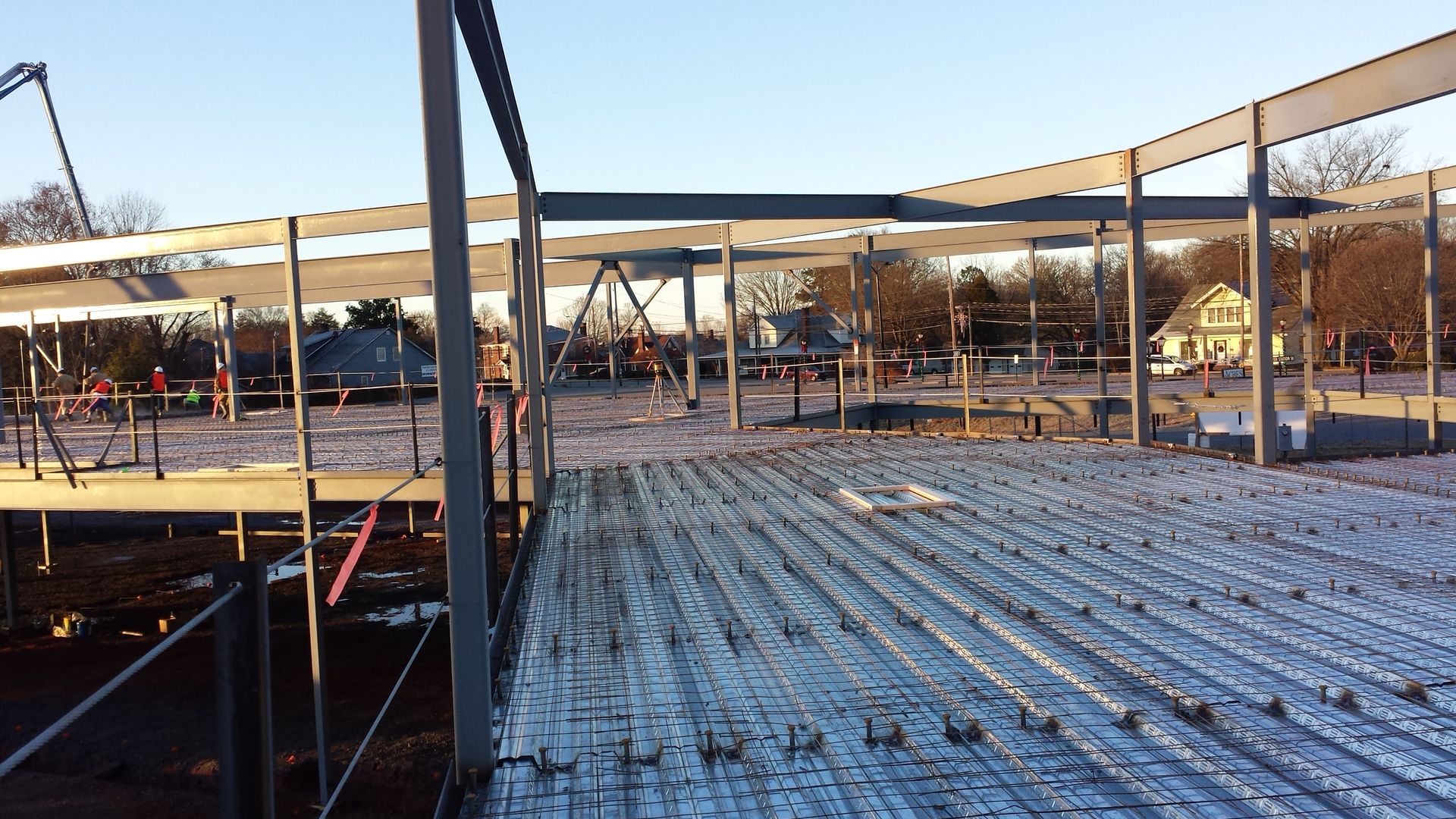 Snow-dusted construction site with steel framework and workers in the distance