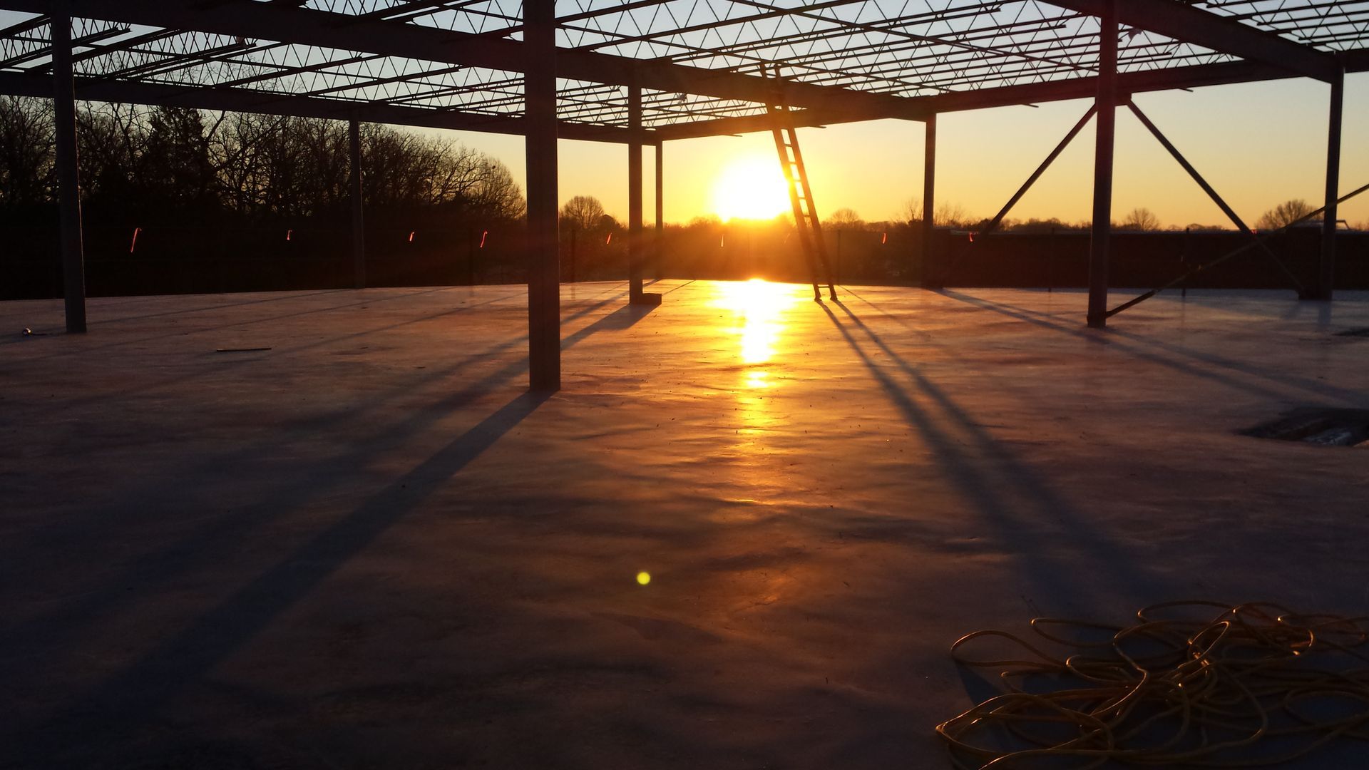 Sunrise over a snow-covered field with long shadows and a metal structure silhouetted in the foreground